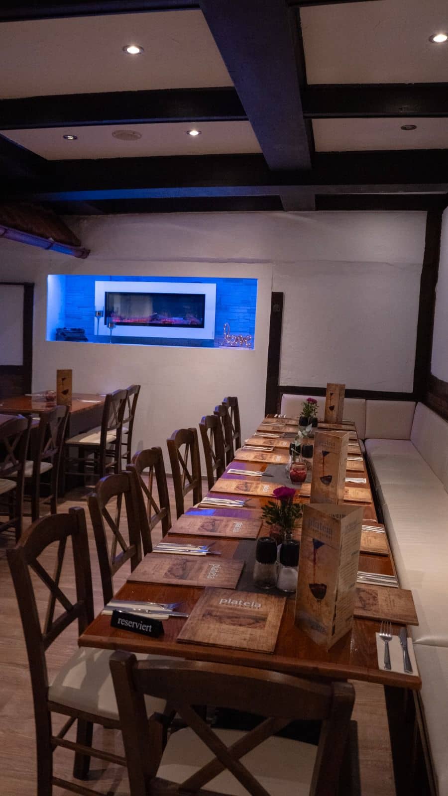Das Foto zeigt einen gemütlichen Innenraum eines Restaurants mit einer langen Reihe gedeckter Holztische und Stühlen, die auf Gäste warten.
